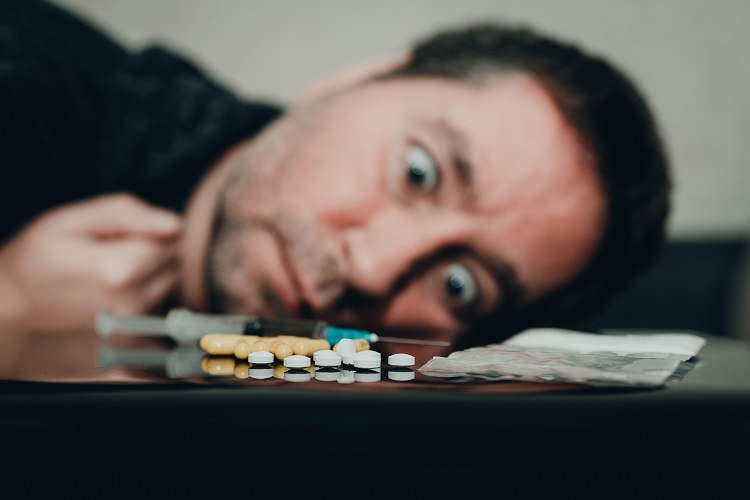 A dejected man lies with his head on the table and feels withdrawal symptoms, a kratom capsule lies in front of him