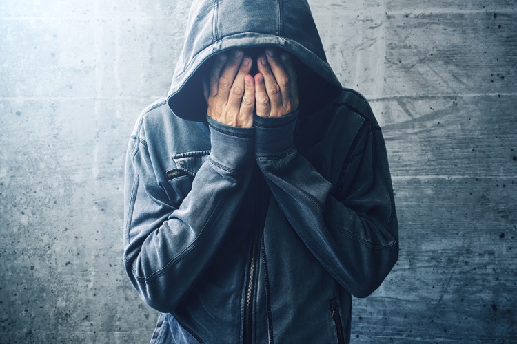 A man in a hood with his hands on his face, indicating anxiety that may be a negative effect of kratom