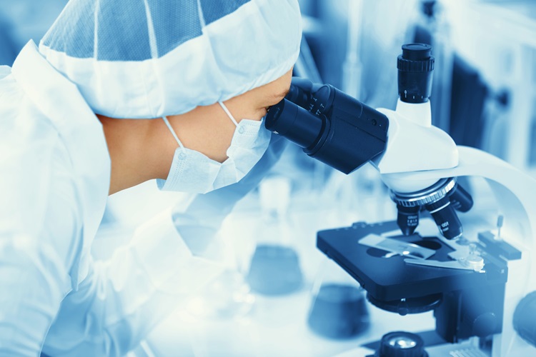 A young doctor examines a microscope slide in the life sciences (e.g., oncology)
