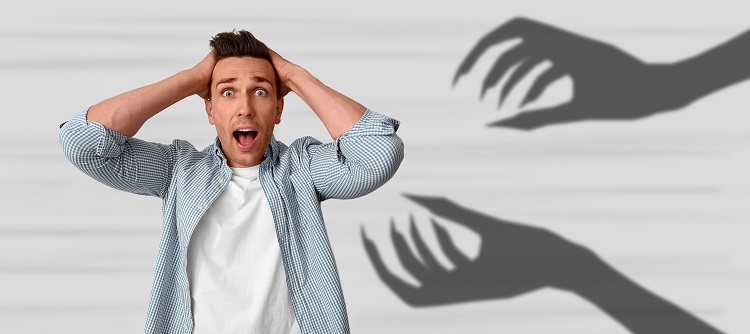 A man holding his head and being frightened, showing his hands as a shadow, depicting paranoia, which is a manifestation of an undesirable effect, i.e. too much HHC 