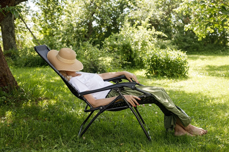 A woman sits outside on a deck chair in the garden with a straw hat over her head and relaxes outside to get rid of the side effects of hexahydrocannabinol